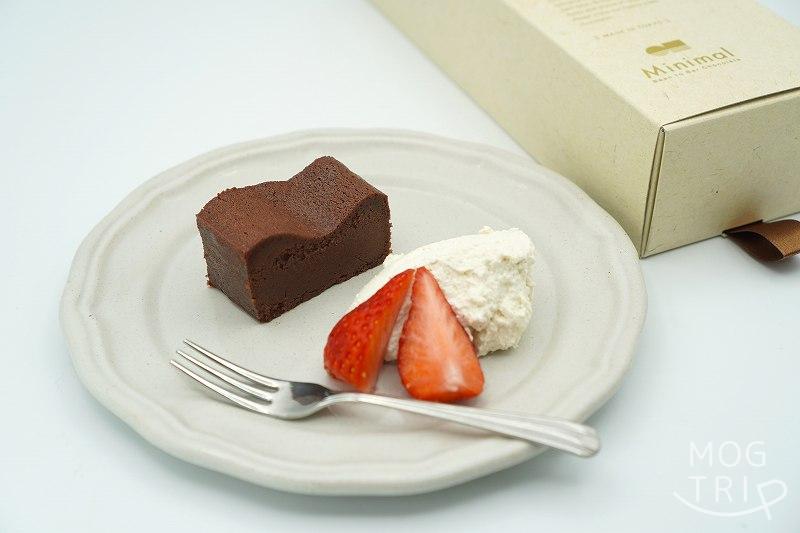 ビーントゥバーチョコレート専門店 Minimaru（ミニマル）の生ガトーショコラが生クリームと苺と一緒にさらに載せられ、テーブルに置かれている