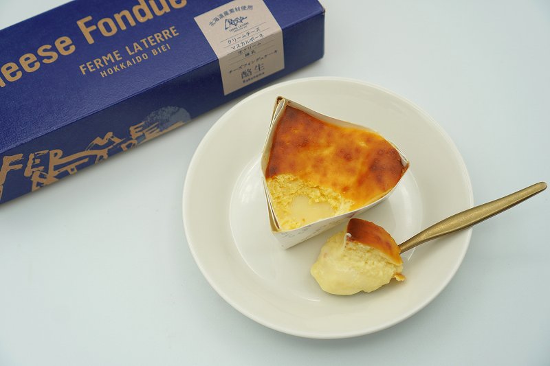 フェルム ラ・テール美瑛のチーズフォンデュケーキ酪生の箱と、お皿に乗せられたチーズフォンデュケーキがテーブルに置かれている