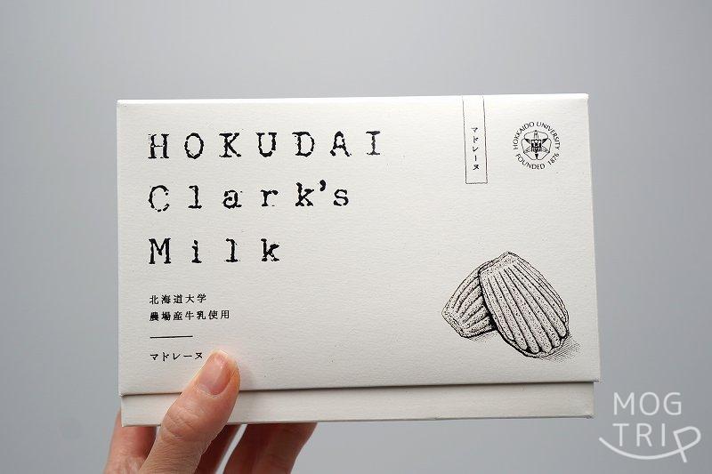 北海道大学の敷地内にある北大マルシェ の「HOKUDAI Clark's Milk マドレーヌ」の箱を手に持っている様子