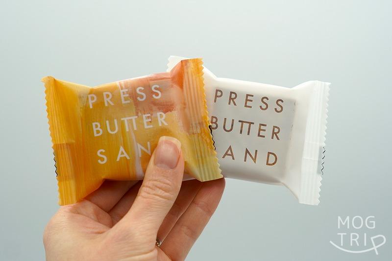 BAKE（ベイク）の「プレスバターサンド」2種類の個包装を手に持っている様子