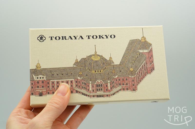 東京駅にある「とらやグランスタ東京店」と「TORAYA TOKYO」の限定品、小形羊羹 夜の梅® 5個入の箱を手に持っている様子
