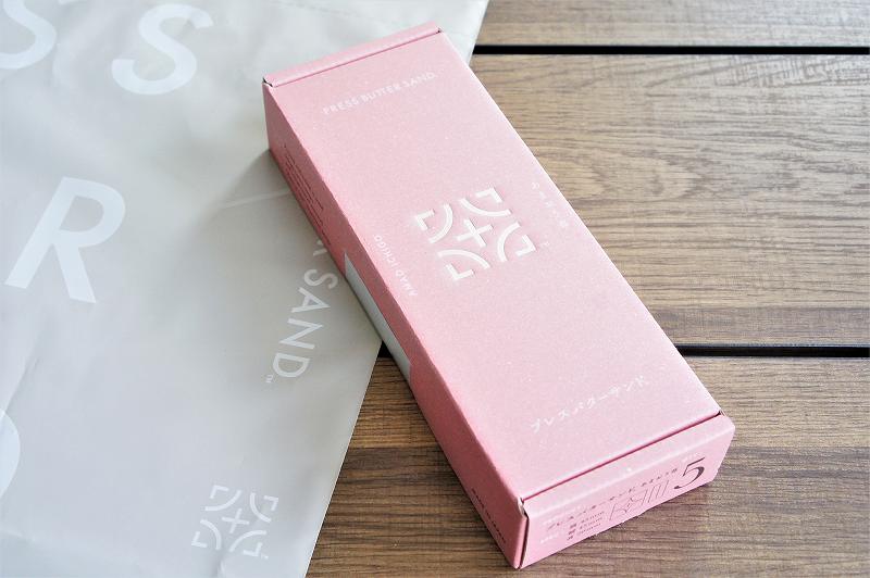 ピンク色の「プレスバターサンド（あまおう苺）」の箱と、袋がテーブルに置かれている