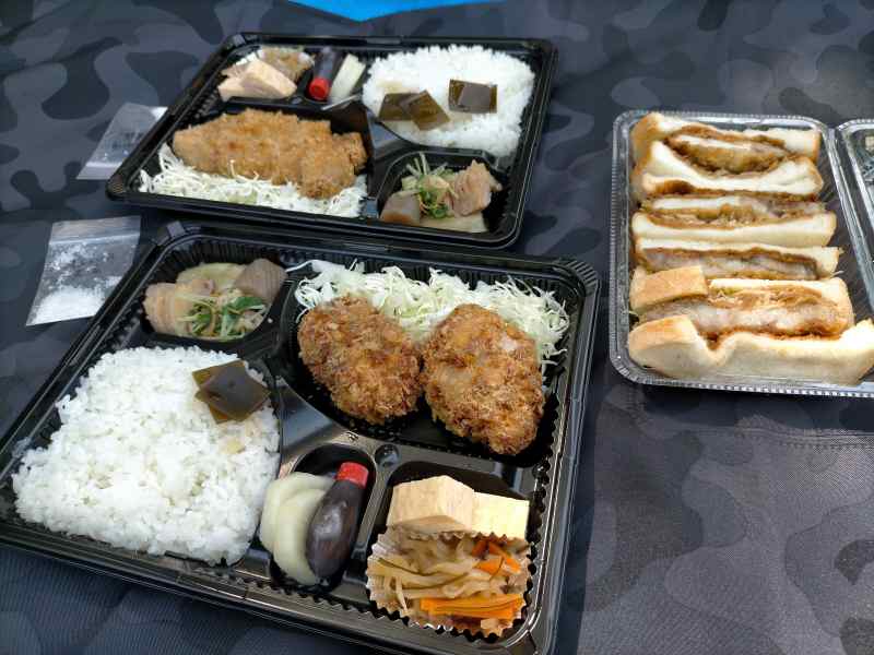 「米愛豚とおばんざい みかみ」のとんかつ弁当やカツサンドが、レジャーシートのうえに置かれている