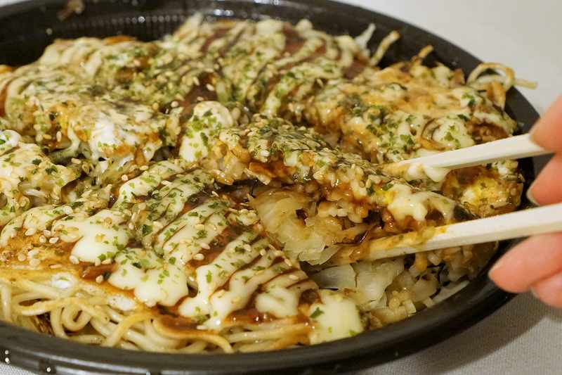 広島お好み焼き ひなちゃんの「タコ肉玉そば」を箸で持ち上げている様子