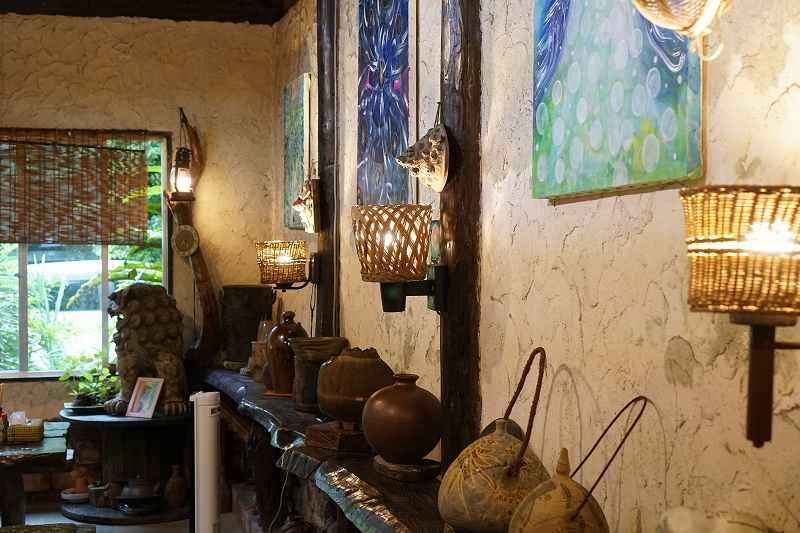 籐のランプシェードや沖縄をおもわせる絵画が飾られた、やちむん喫茶シーサー園の内観