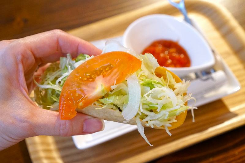 トマトやキャベツなど 野菜がたっぷりはいった「沖縄タコス」を手に持っている様子