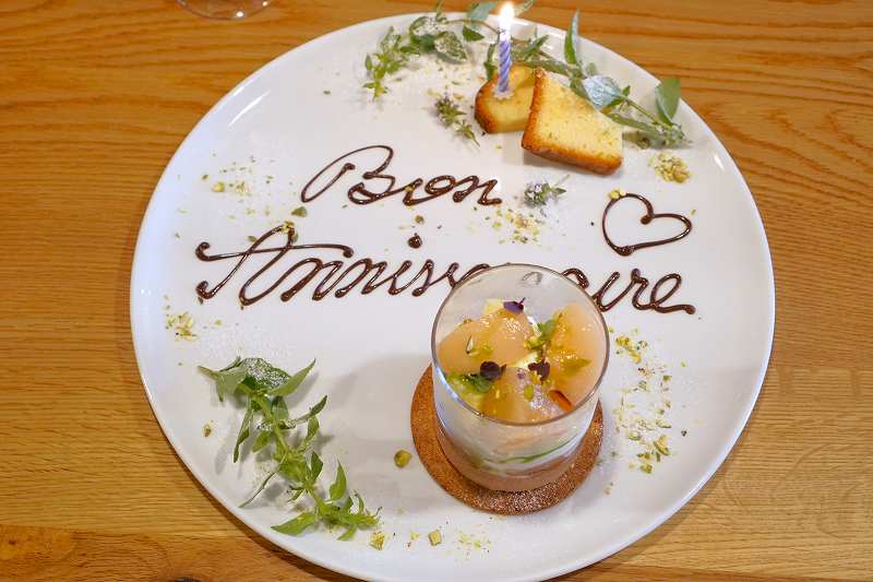 “Bon anniversaire” と書かれた誕生日のデザートプレートがテーブルに置かれている