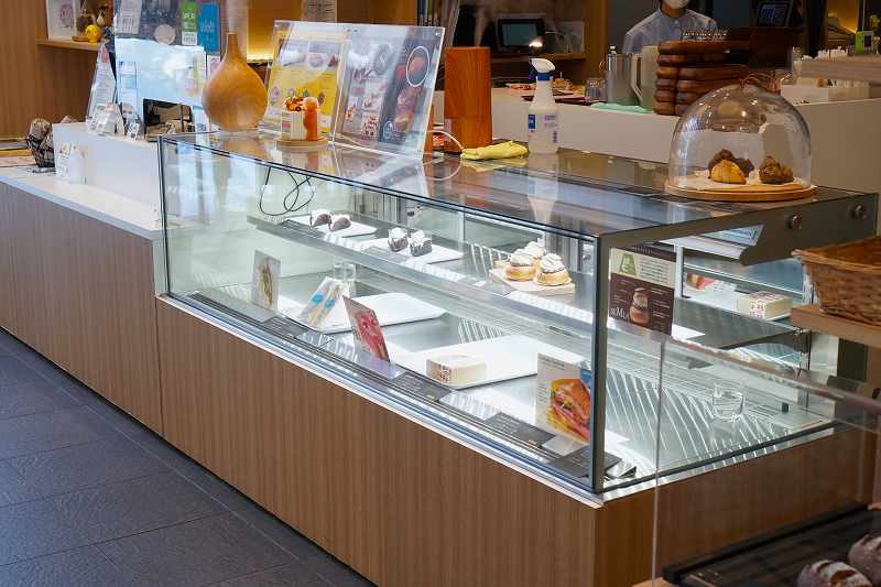ガラスの冷蔵ケースにケーキやサンドイッチなどが並べられている「FIKA CAFE Lagom（ラゴム）」の内観