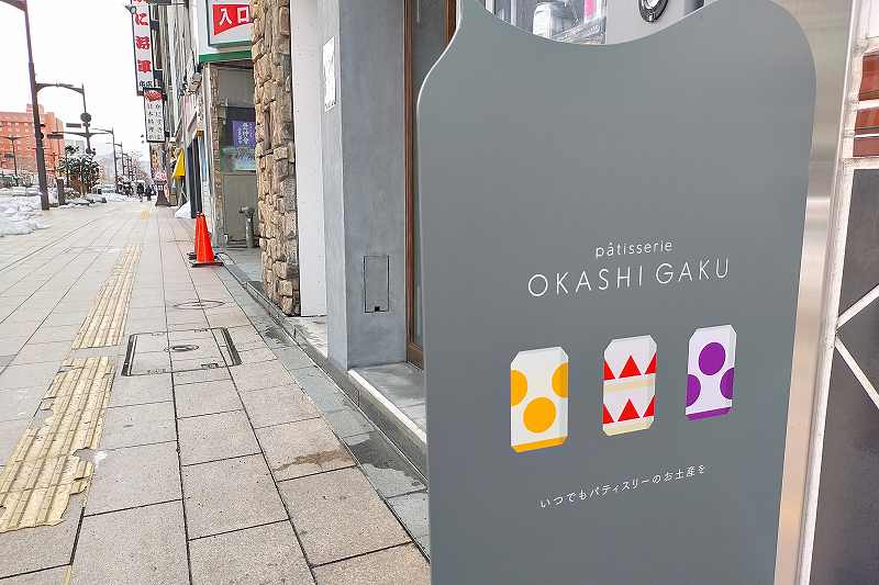 OKASHI GAKU（オカシガク）の看板が地面に置かれている