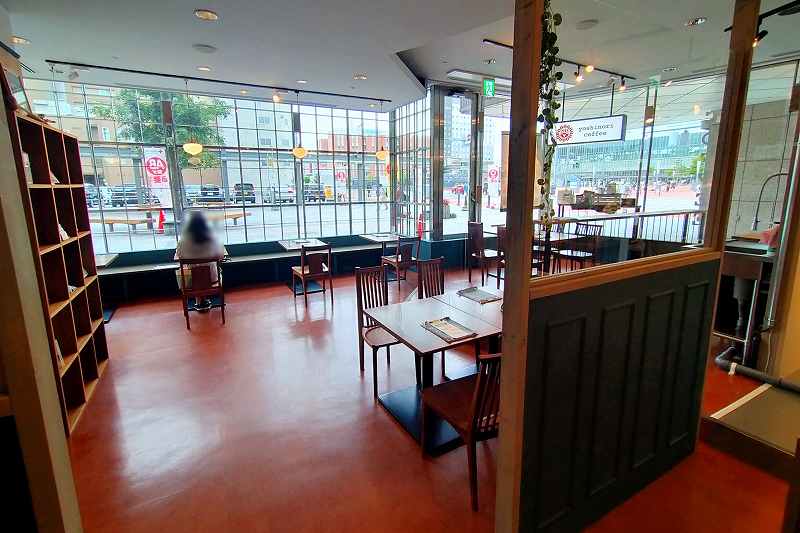 ヨシノリコーヒー旭川駅前店の店内に木のテーブルと椅子がたくさん並べられている