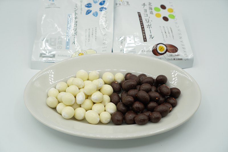 お皿にのせられた共成製菓のチョコ’豆ボールのチョコレート味とミント味の袋がテーブルに置かれている