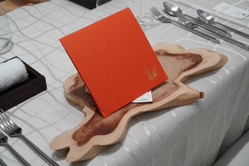 オレンジの封筒と木のトレイ、カトラリーなどがテーブルに置かれている