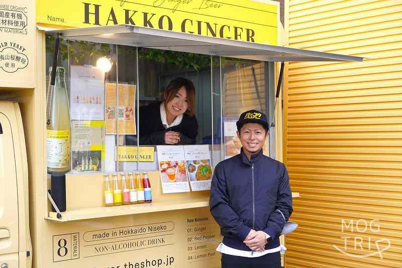 HAKKOGINGERのキッチンカーの中に女性スタッフさん、前に代表・前田さんが笑顔で立っている