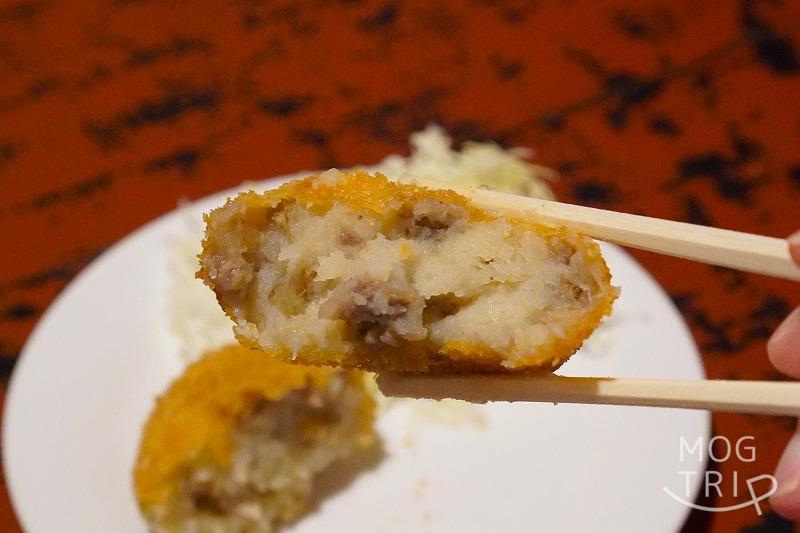 函館にある「すき焼き専門店 阿さ利 本店」の、揚げたてコロッケを箸で持ち上げている様子