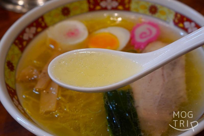 「函館塩ラーメン しなの」の、塩ラーメンのスープをれんげですくっている様子