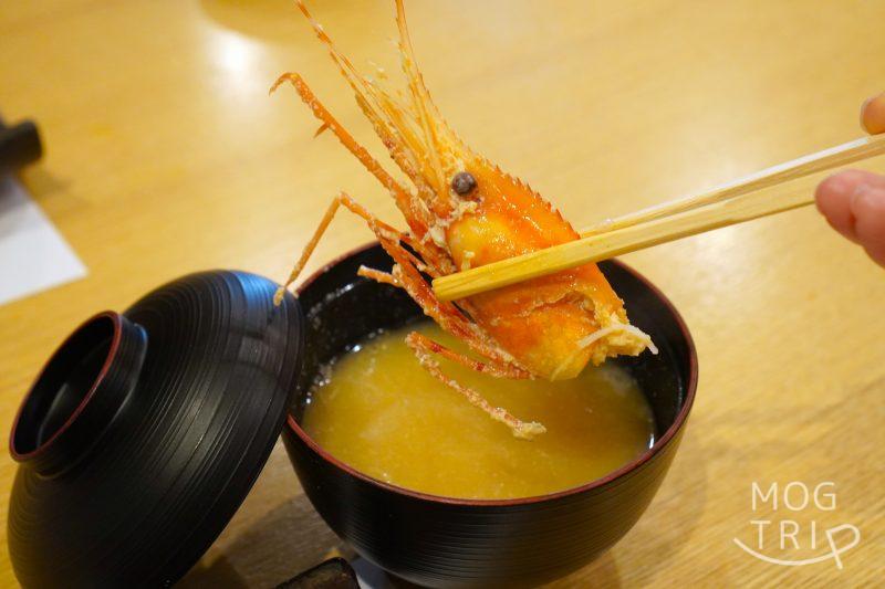 旭川「小西鮨」の牡丹海老の頭汁に入っている、牡丹海老の頭を箸で持ち上げている様子